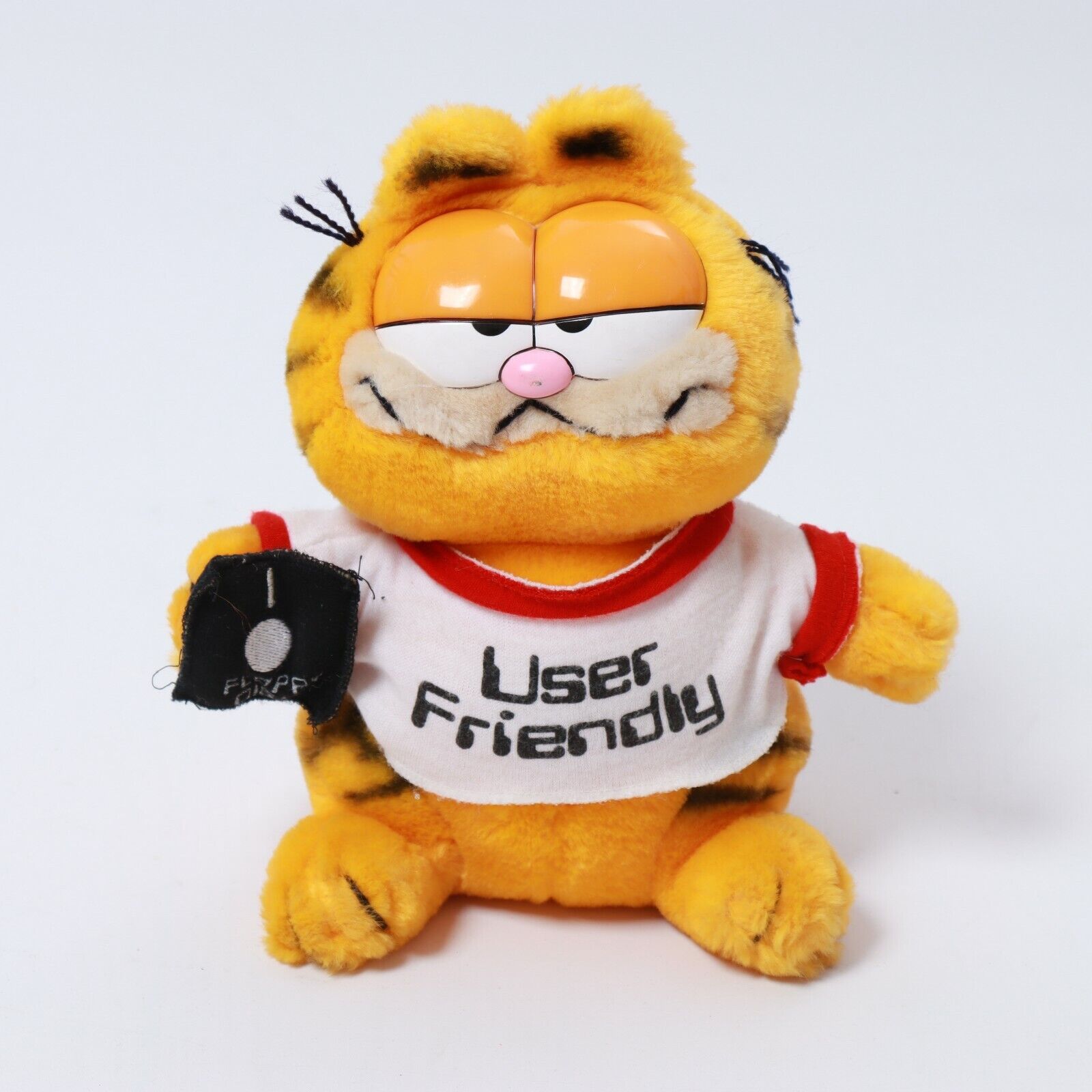 A plush of Garfield the cat holding a floppy disk and wearing a t-shirt with the text 'user friendly'.